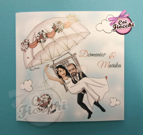partecipazione-con-caricatura manga degli sposi che si lanciano con un paracadute ricco di festoni e fiori di orchidea e rose color pesca