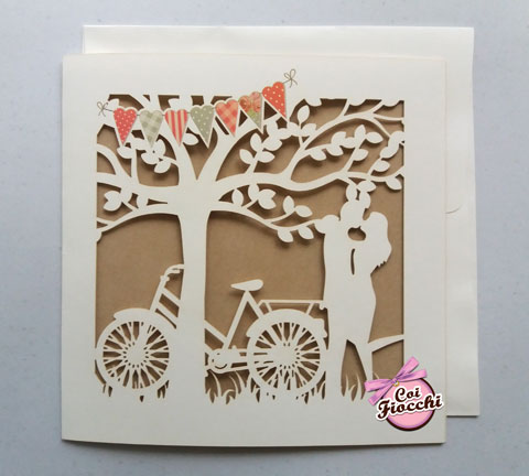 partecipazione nozze lasercut con sposi che si baciano sotto l'albero e bicicletta